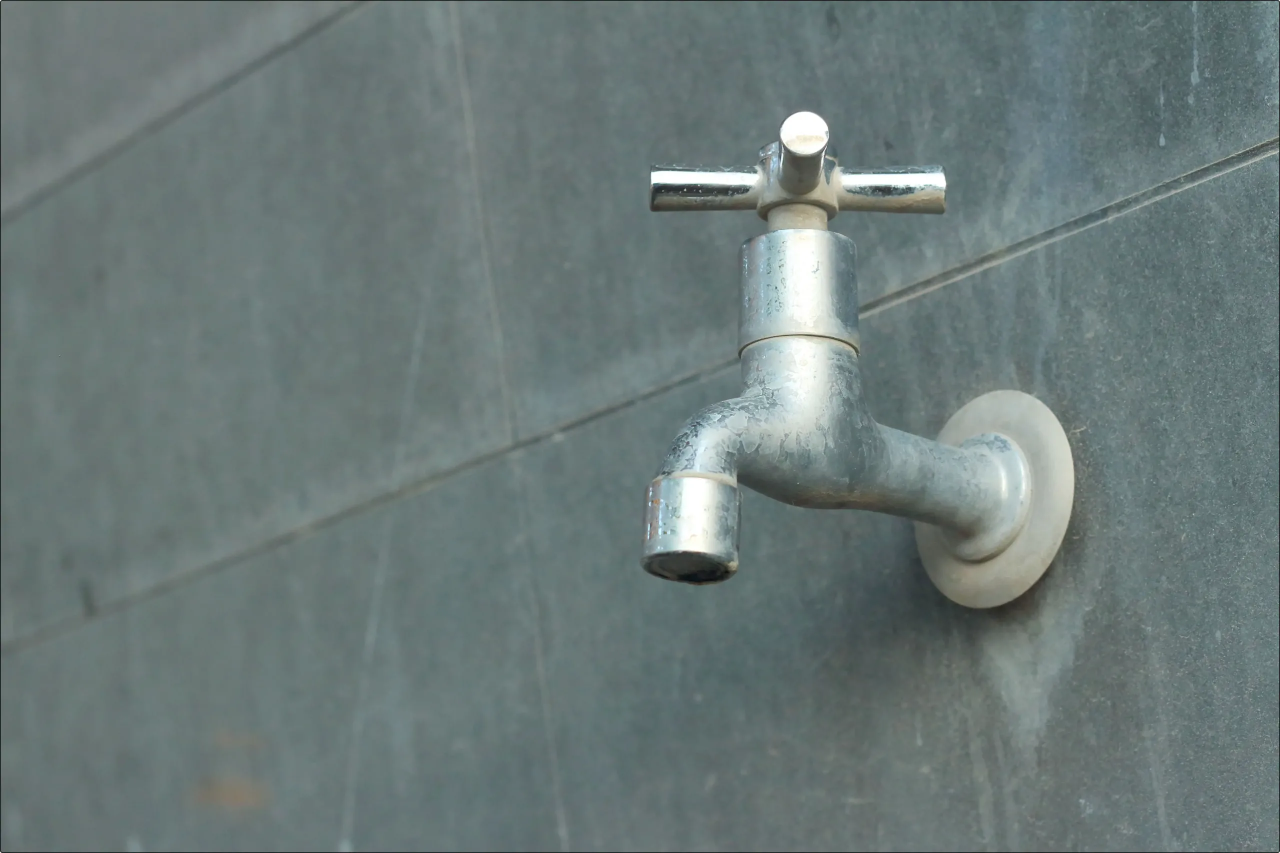 Metal tap on grey wall with watermarks on the pipe