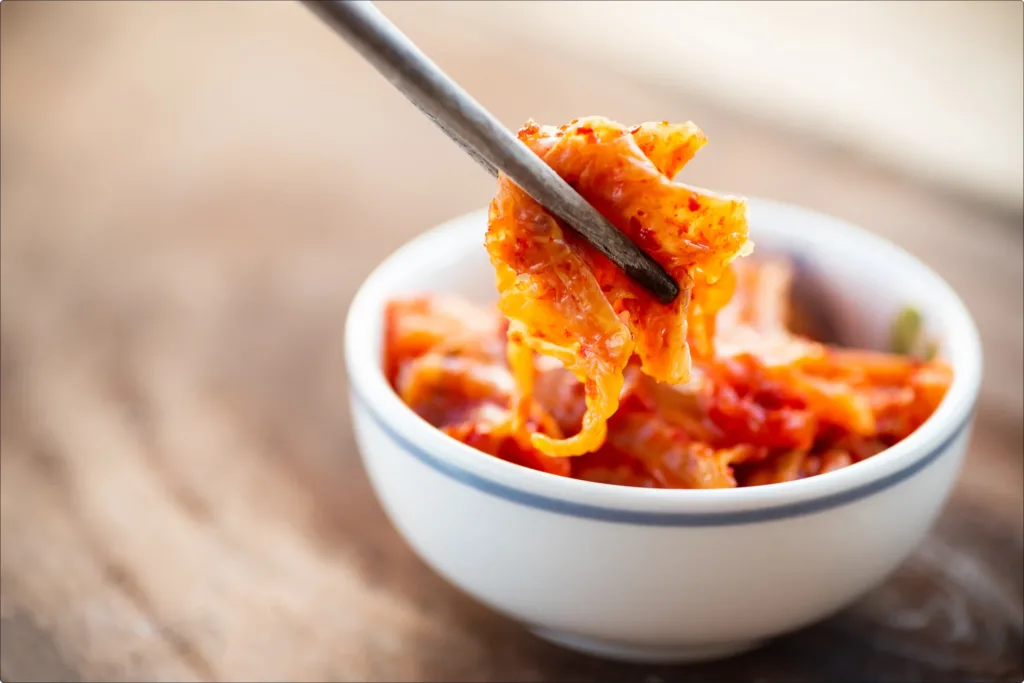 Kimchi in a bowl on a wooden table with chopsticks