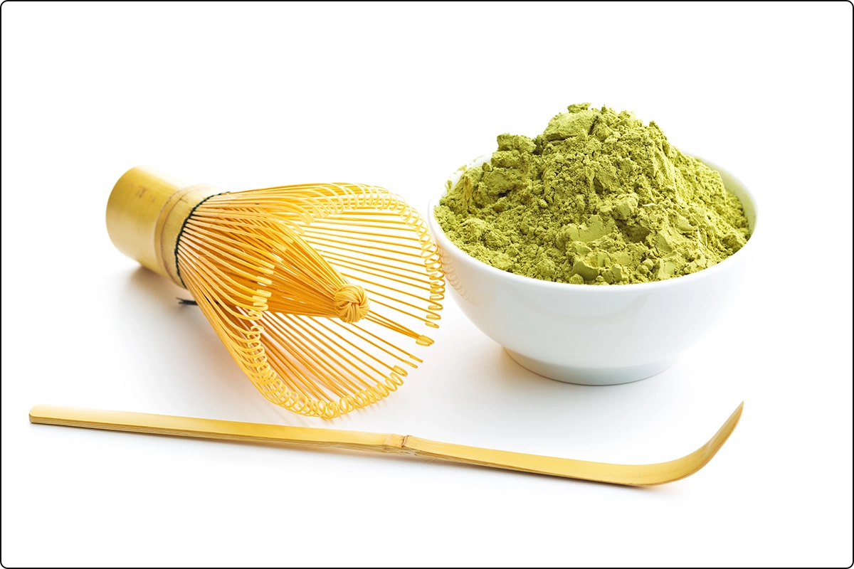 japanese green tea powder in small bowl next to bamboo whisker on white surface