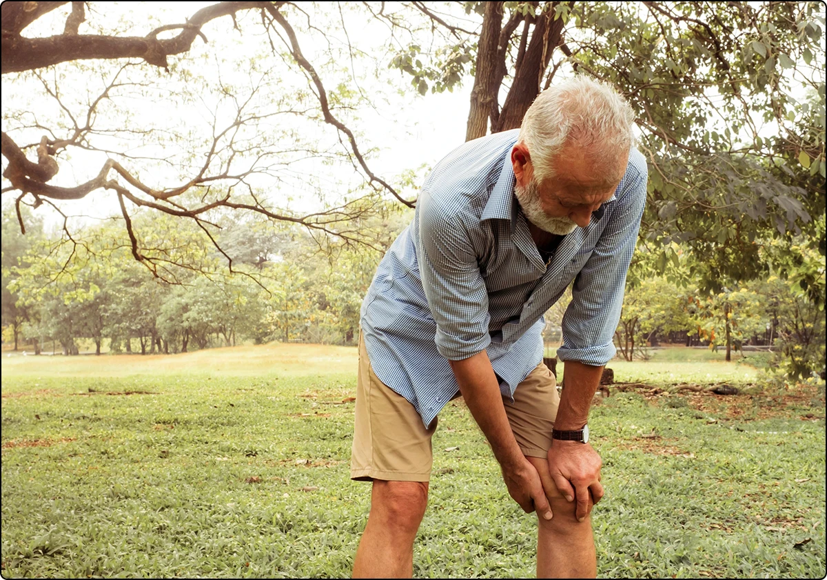 older man in nature park holding knee in pain