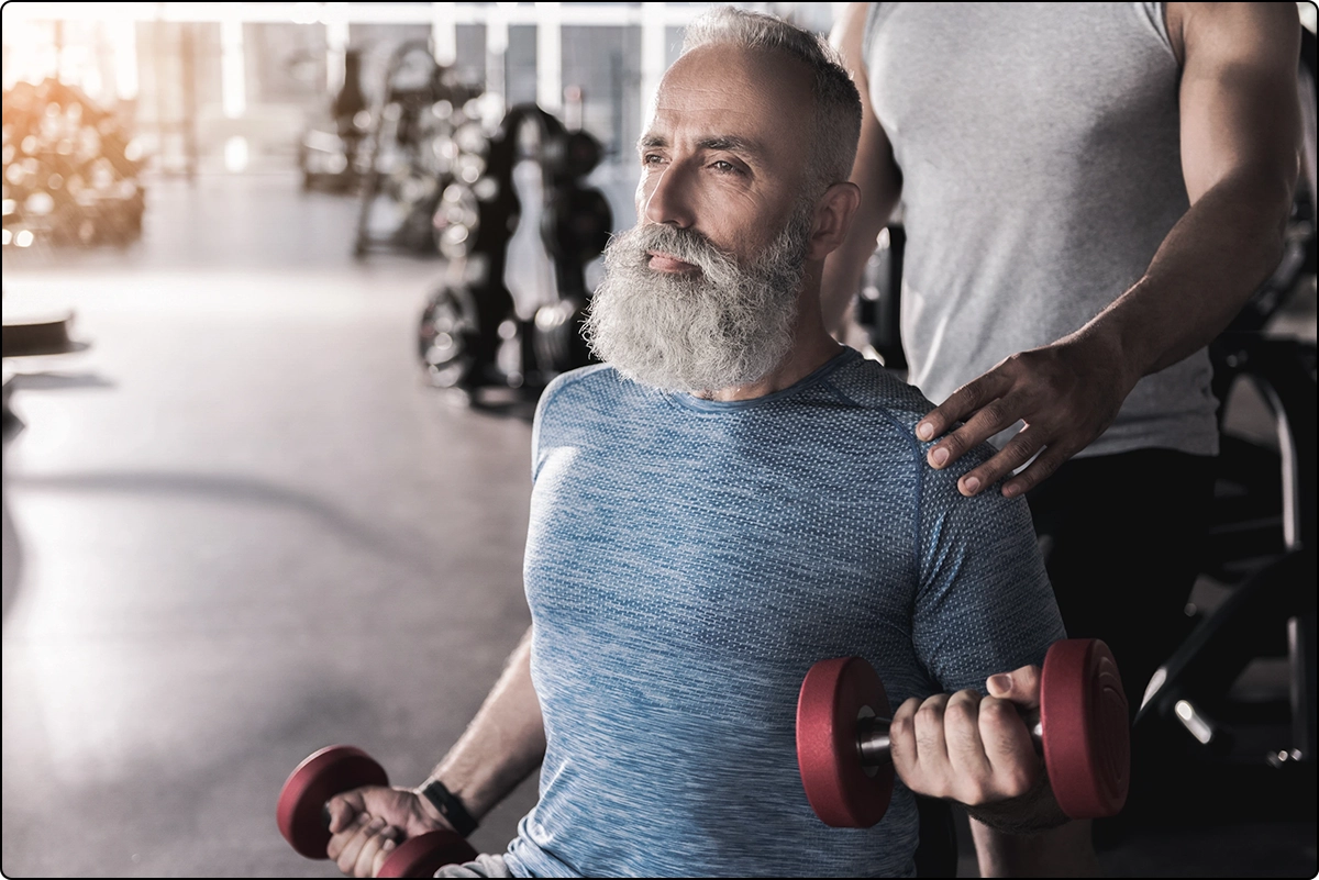 healthy strong bearded senior man in gym doing bicep curls, muscle strength benefit (after vitamin d cancer)
