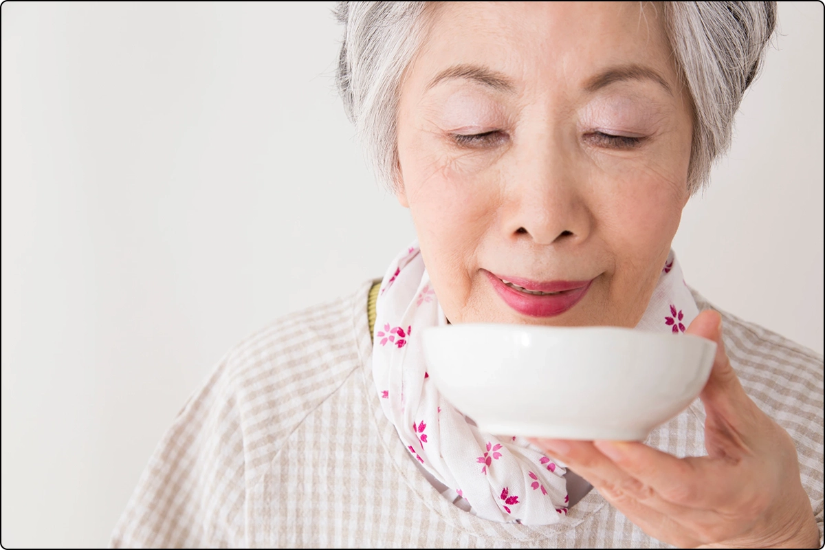 senior asian woman with healthy skin (adk) drinking from a bowl