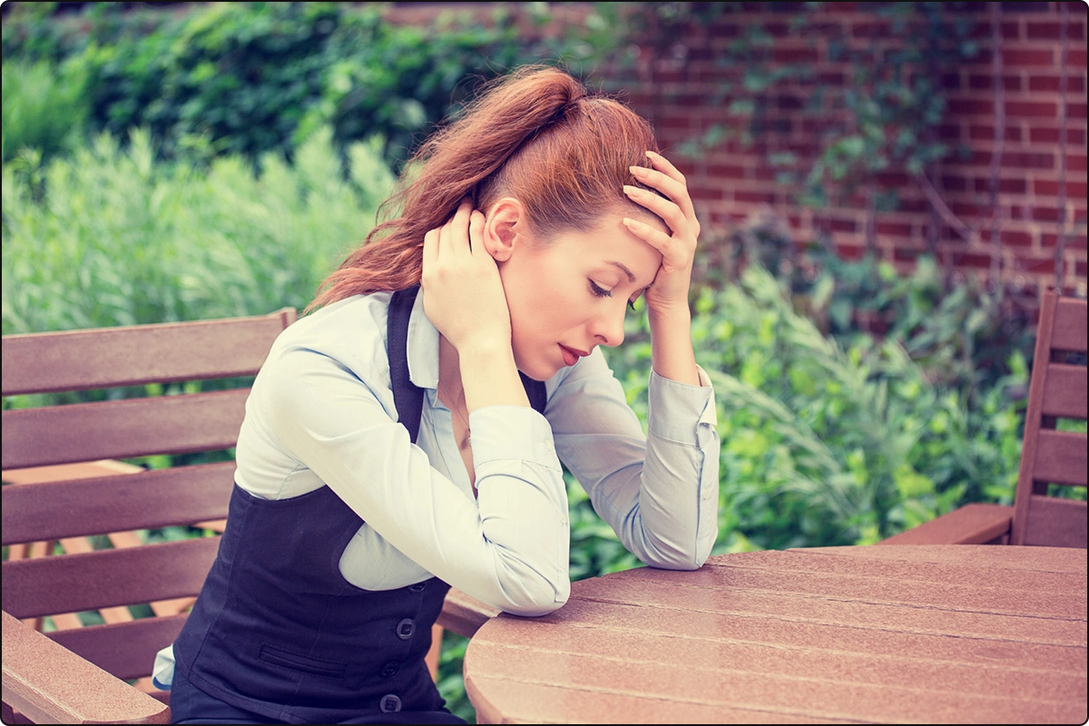 stressed out woman sitting at table in garden area, stress requires more immune support